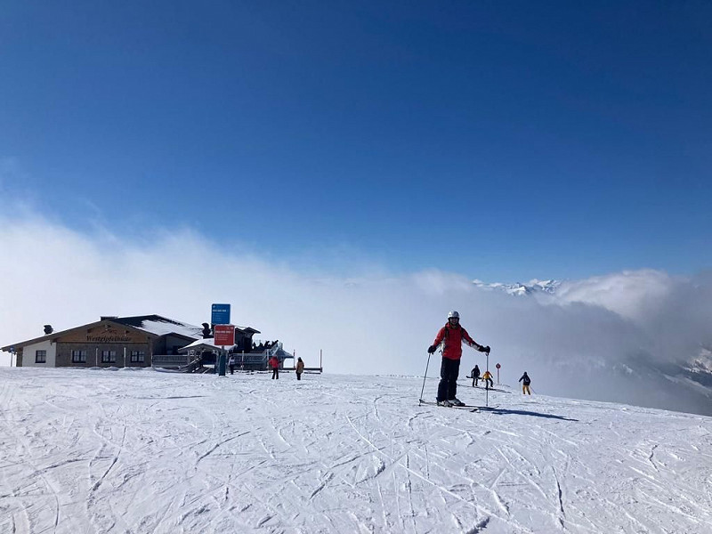 Skier leading group across snow field. Blue sky, ski hut in background.